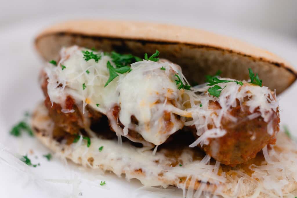 homemade meatball sub with three meatballs on sourdough bread covered in cheese and sprinkled with parsley