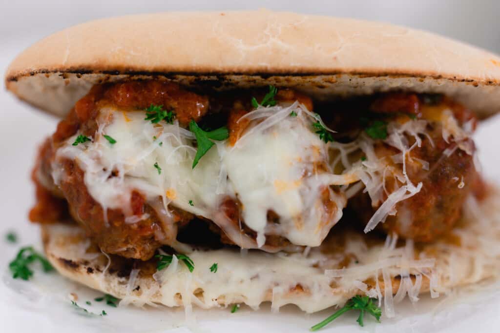 three meatballs covered in sauce, cheese and parsley on a homemade sourdough hoagie