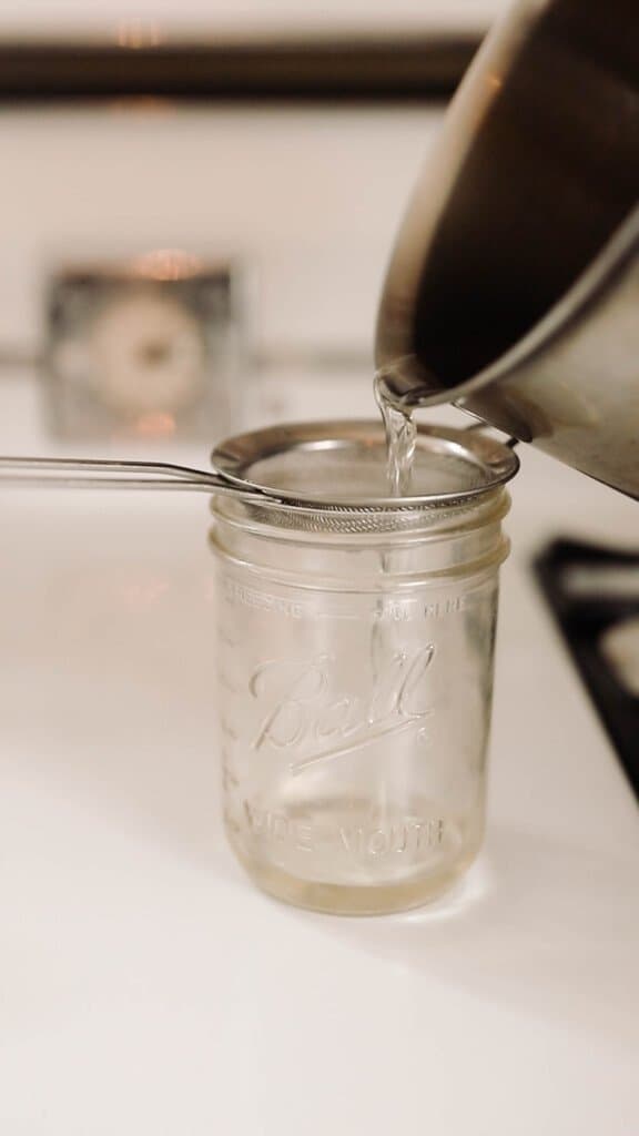 pouring rendered beef fat into a mason jar through a fine mesh stainer. Jar is on an antique white stove