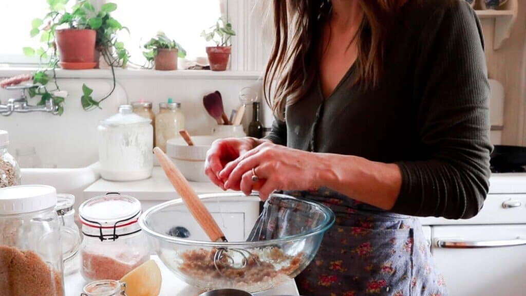 women cracking egg into sugar in a glass bowl to make muffins