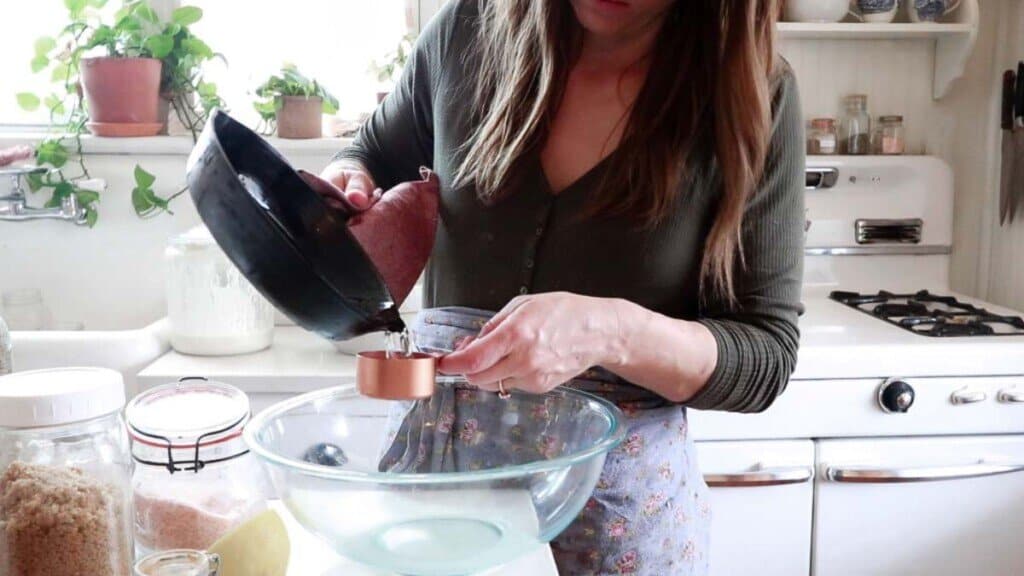 women pouring melted coconut oil into a measuring cup above a glass bowl