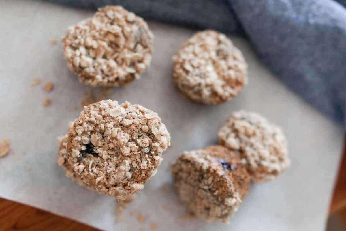 sourdough blueberry muffins on a wire rack on a white countertop with blueberries scattered around on the counter. The front muffin is sliced in half.