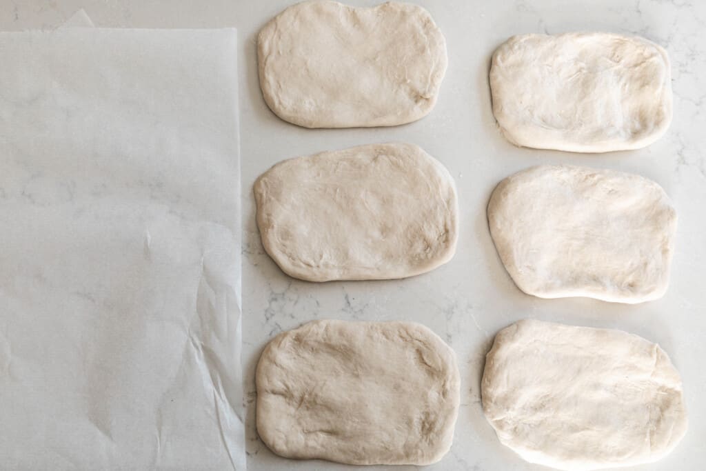 6 sourdough bread dough patted out on a white countertop ready for shaping