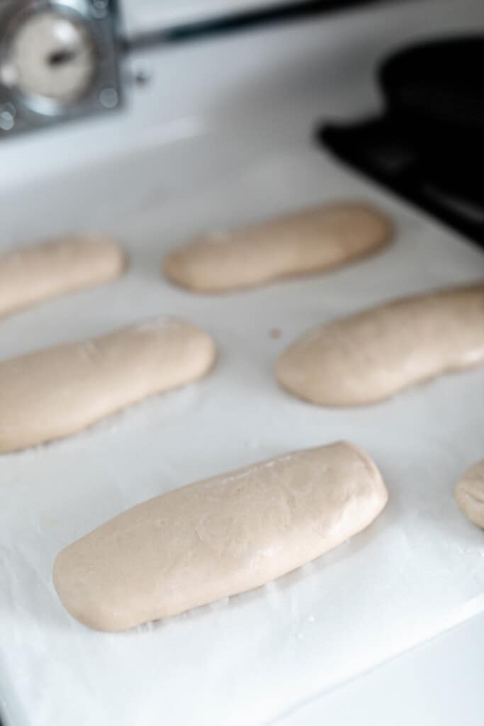 sourdough hoagie rolls on parchment paper for rising on a antique stove