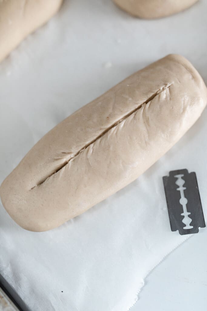 sourdough sandwich roll dough on parchment paper with a scoring tool to the right