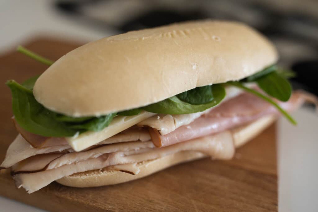 sourdough sandwich with deli meat, cheese, and spinach on a wood cutting board