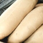 sourdough sandwich rolls in a basket with a blue and white stripped towel on the side