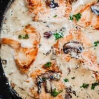 cast iron skillet with seared chicken breast and mushrooms in a cream sauce with fresh herbs on top