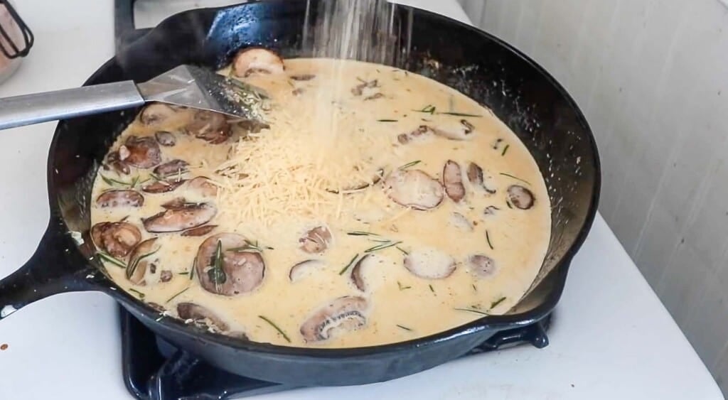 parmesan being added to creamy mushroom sauce in a cast iron skillet