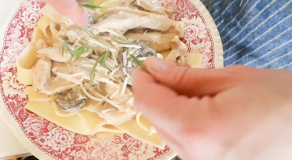 hand sprinkling fresh rosemary onto creamy chicken and mushroom pasta