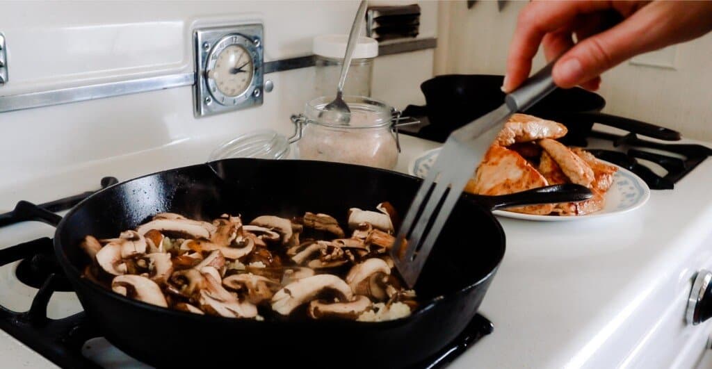 mushrooms being sautéed in a cast iron skillet on an white antique stove