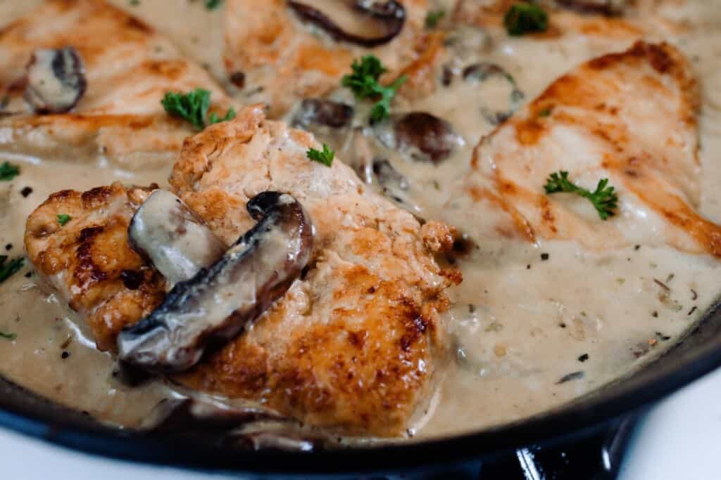 close up picture of seared chicken in a creamy mushroom sauce with herbs in a cast iron skillet.