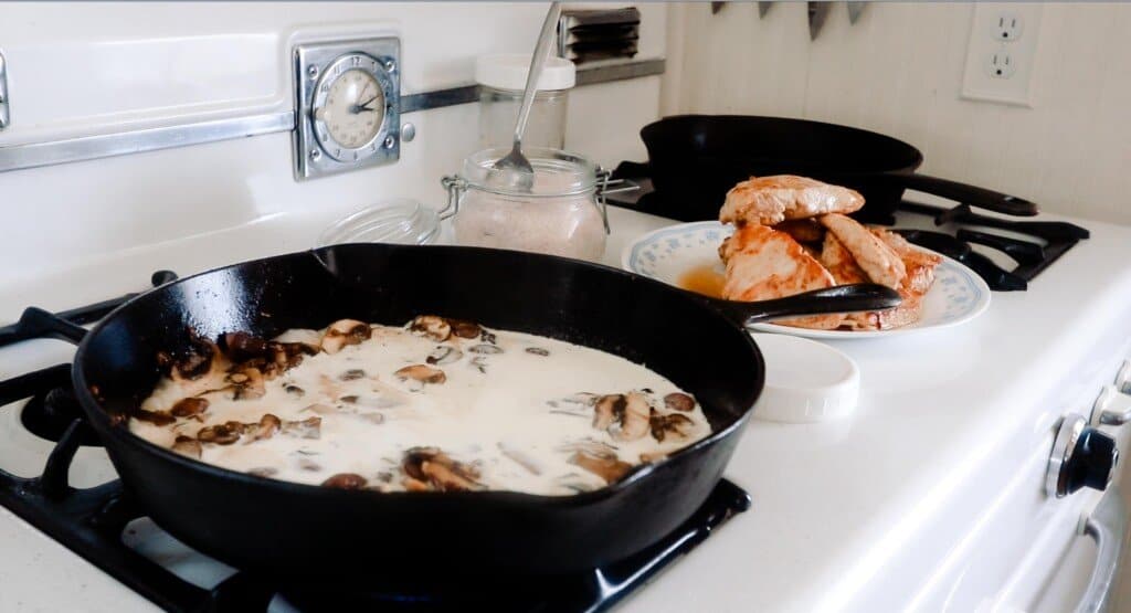 cream added to mushrooms in a cast iron skillet on an antique stove