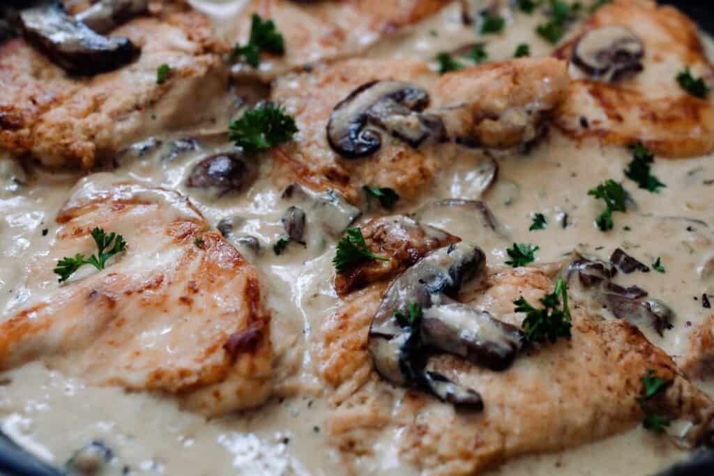 close up picture of seared chicken breast in a creamy mushroom sauce with herbs