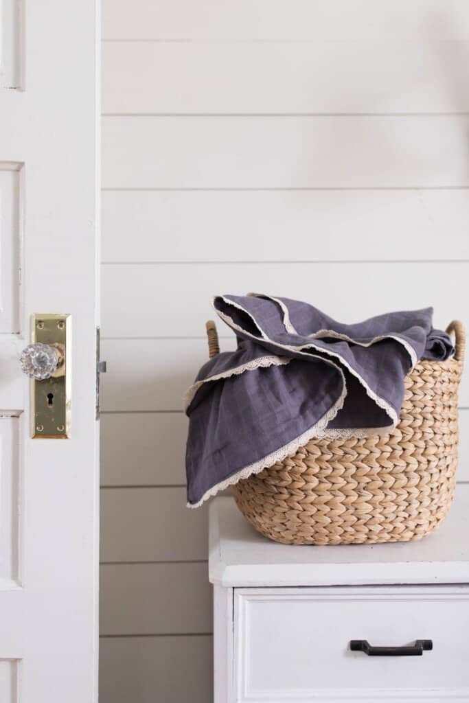 a navy DIY gauze swaddle in a wicker basket on a white nightstand