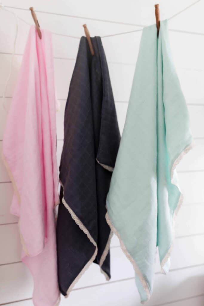 a pink, navy, and teal gauze swaddle blanket with lace hangin with clothespins on string