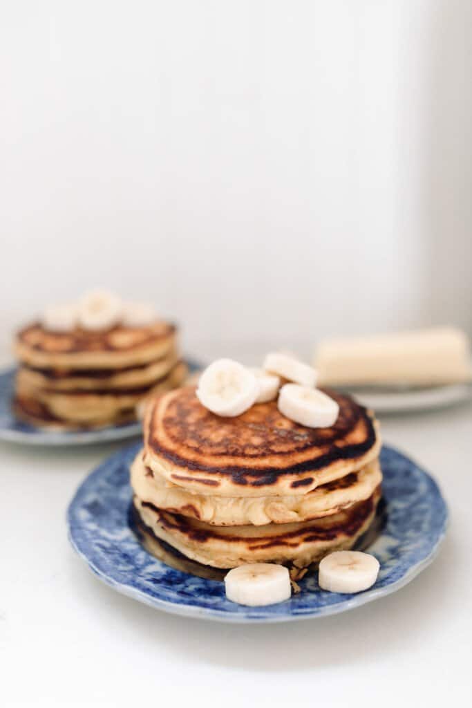 two stacks of pancakes with bananas on blue plates on a white countertop