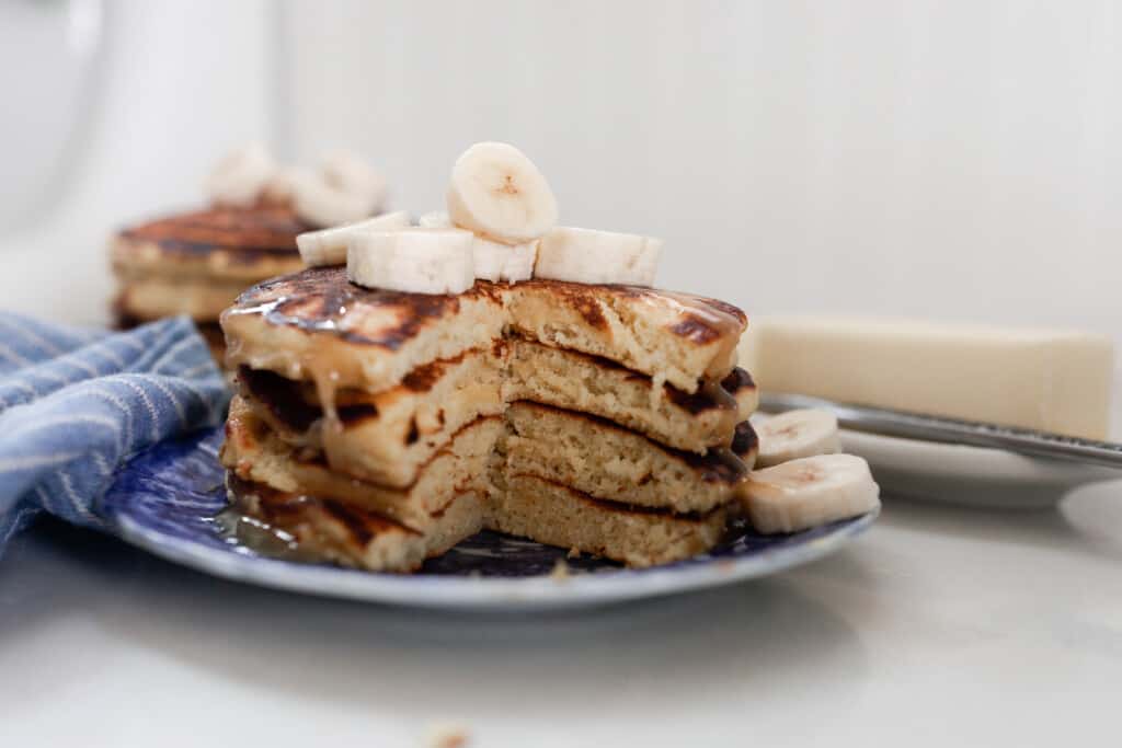 two stacks of einkorn pancakes with bananas on a white and blue antique plate on a white countertop