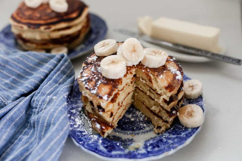 a stack of fluffy einkorn pancakes topped with syrup and sliced banana on a antique blue and white plate with another stack in the background