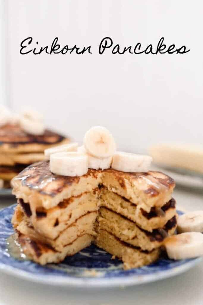 stack of einkorn pancakes topped with bananas on a blue and white antique plate. Butter on a dish is in the background