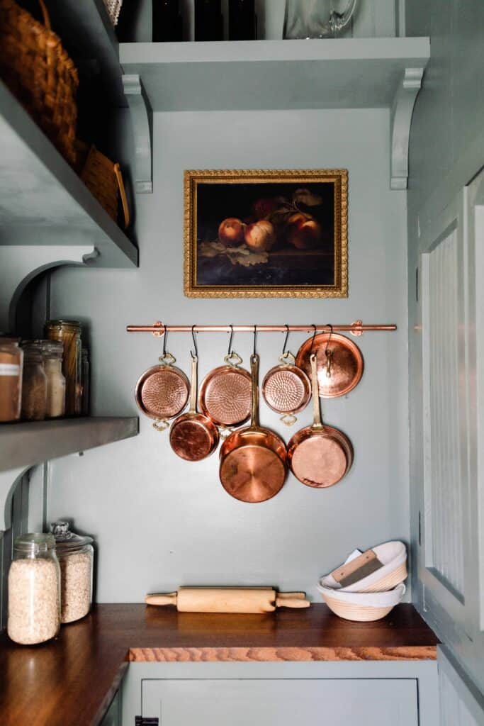 victorian farmhouse pantry with blue green walls, cabinets with wood countertops, shelving, and copper pots handing on the wall