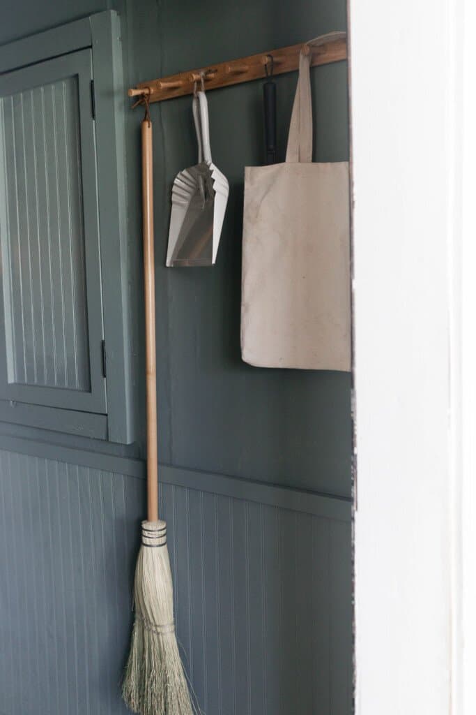 peg rail against a blue green wall with a handmade broom, white dustpan and canvas tote hanging on the pegs