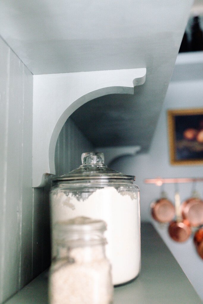 jars of flour on a wooden shelve with another shelf hung with corbels above