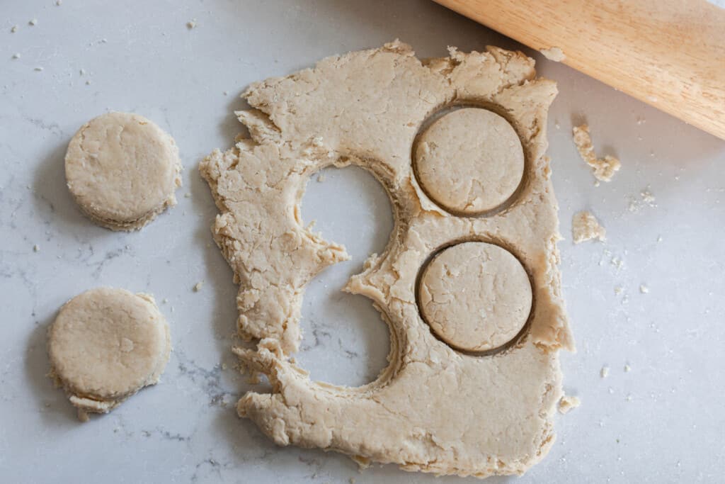 sourdough biscuit dough rolled out on a white quarts countertop and four biscuits cut out