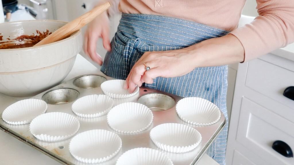 women wearing a blue apron placing cupcake liner into muffin tin wells