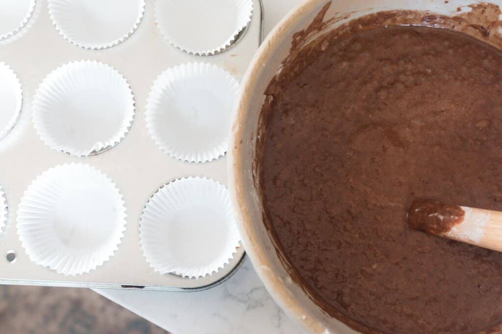 sourdough chocolate cupcake batter in a large bowl next to muffin tins filled with liners
