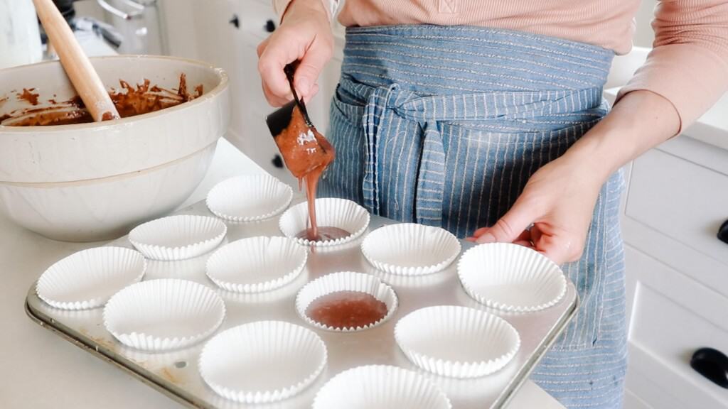 women wearing a blue stripped apron pouring sourdough cupcake batter into lined muffin tins