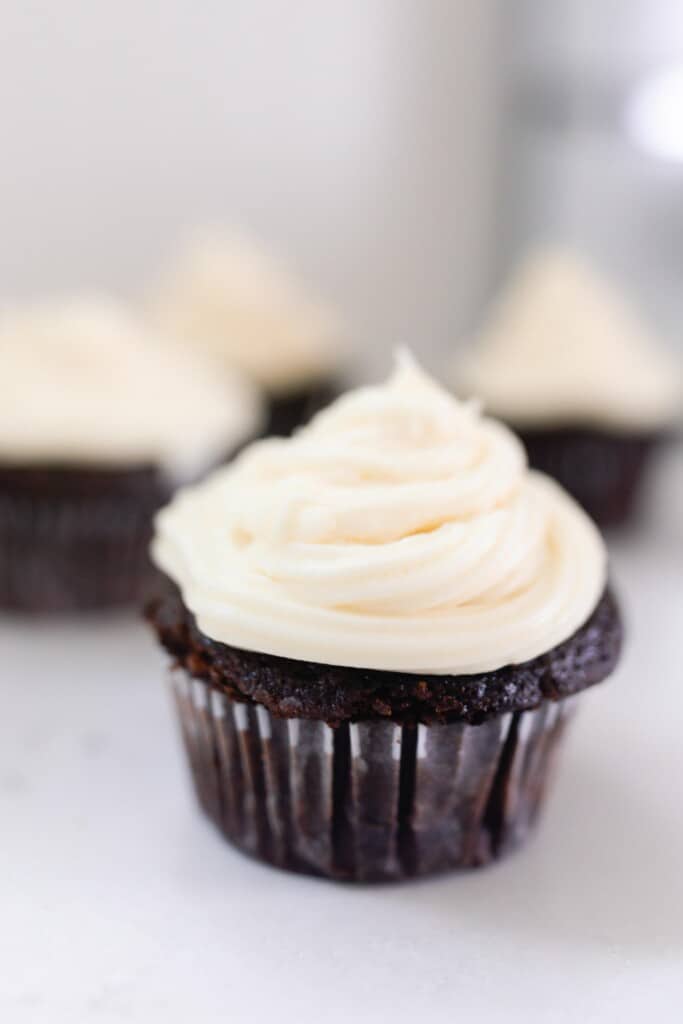 sourdough chocolate cupcake with white frosting on a antique stove with more cupcakes in the background