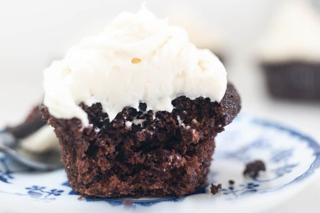 sourdough chocolate cupcake with white frosting cut in half on a white and blue antique plate