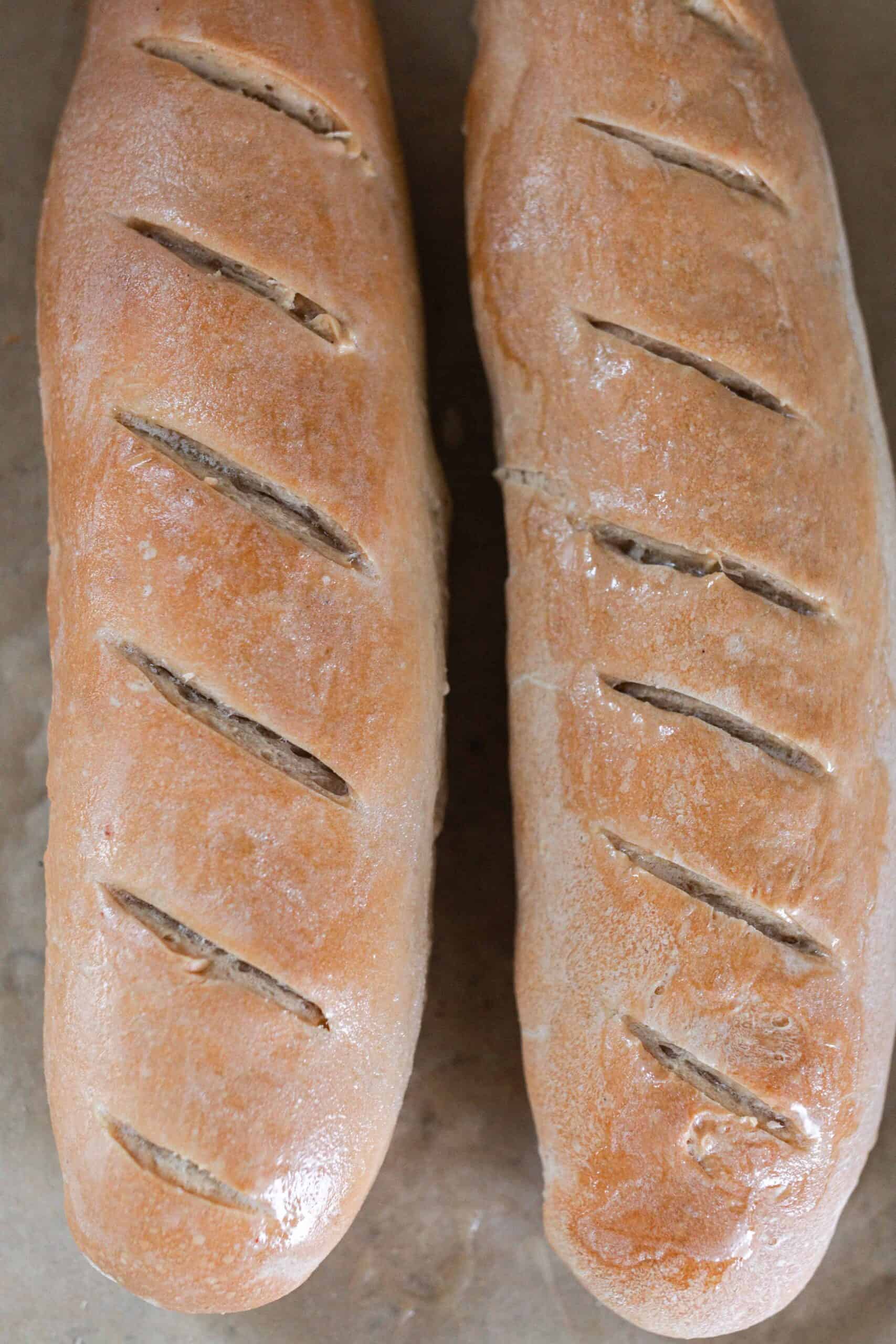 overhead photo of two baked sourdough French breads on parchment paper.