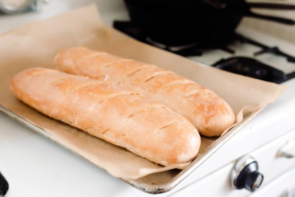 sourdough French bread baguettes on a parchment lined baking sheet on top of a vintage oven.