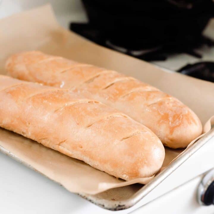 sourdough French bread baguettes on a parchment lined baking sheet on top of a vintage oven.