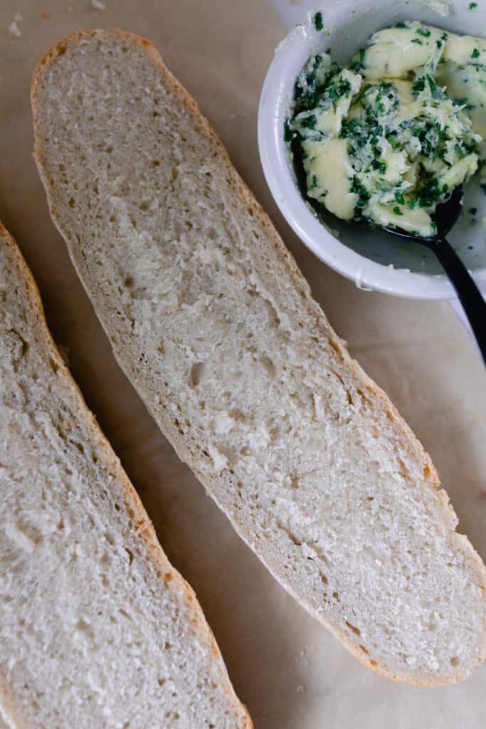 sourdough French bread cut in half with a bowl of garlic butter in the back corner