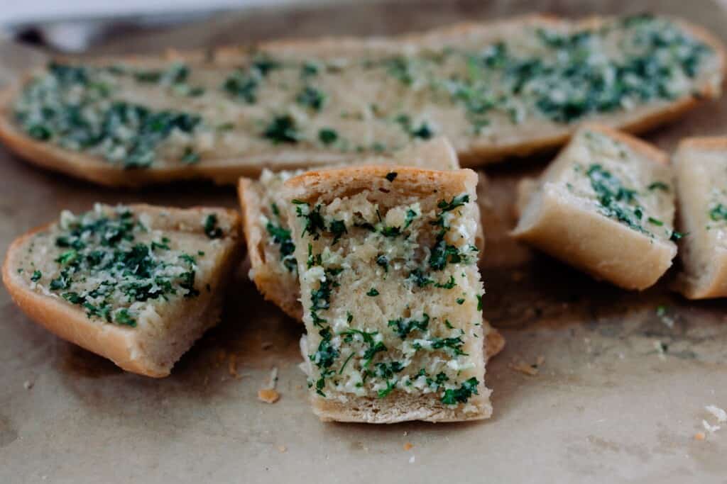 slices of sourdough garlic bread on parchment paper with a half of garlic bread in the background