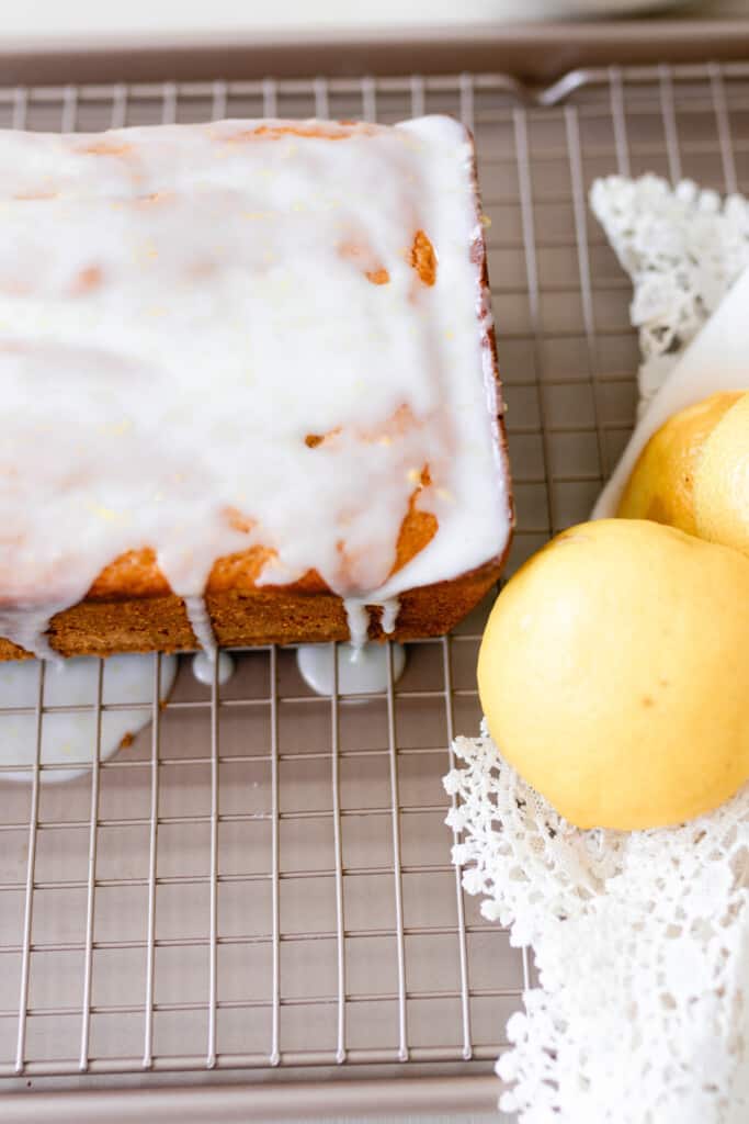 overhead photo of lemon sourdough pound cake covered in lemon icing on a white rack with a white lace towel with lemons on top to the right