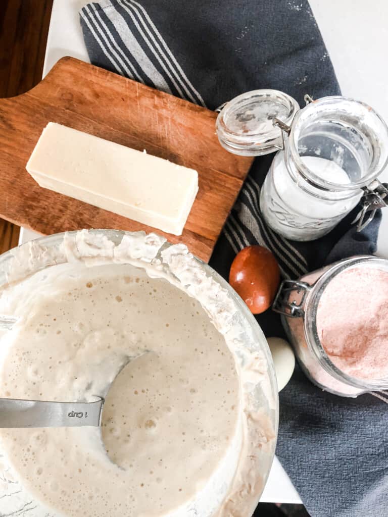 sourdough cheddar waffle ingredients: sourdough starter, salt, baking soda, cheese on a wood cutting board, and eggs