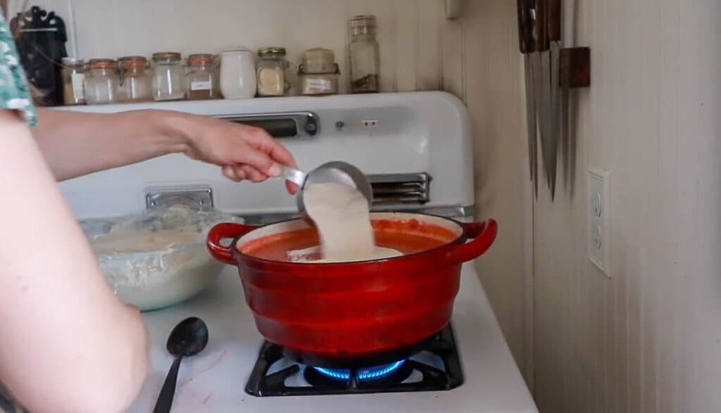 women adding pectin to a red pot full of pureed strawberry