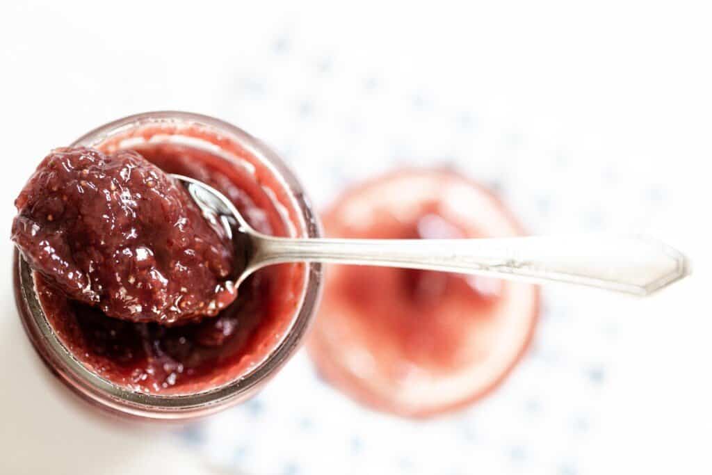 jar of strawberry jam with a spoon full of jam resting on the rim.