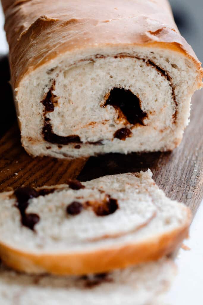 loaf of sourdough cinnamon raisin bread with a cinnamon raisin swirl on a cutting board with a slice of bread in front of the loaf