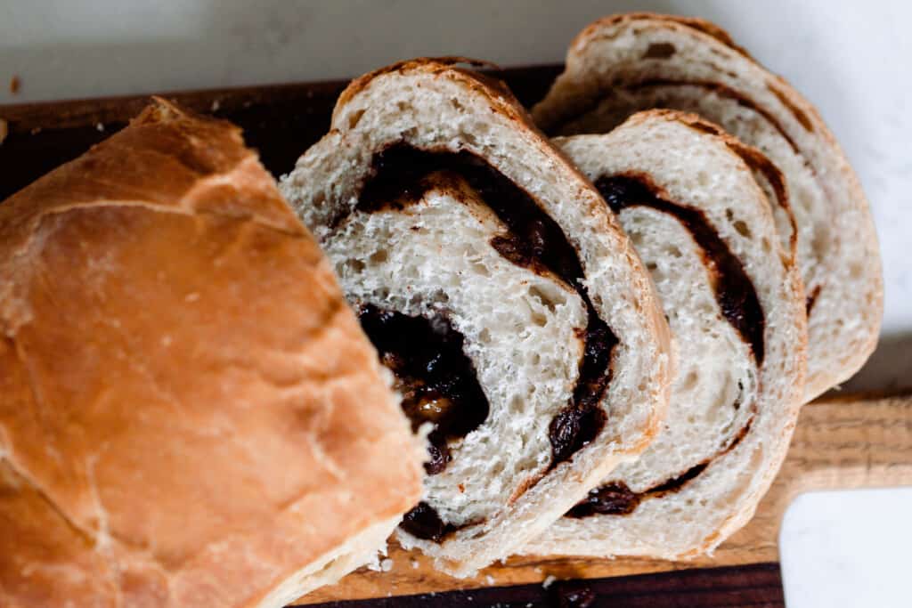 overhead photo of a loaf of sourdough raisin bread sliced on a wood cutting board on a white countertop