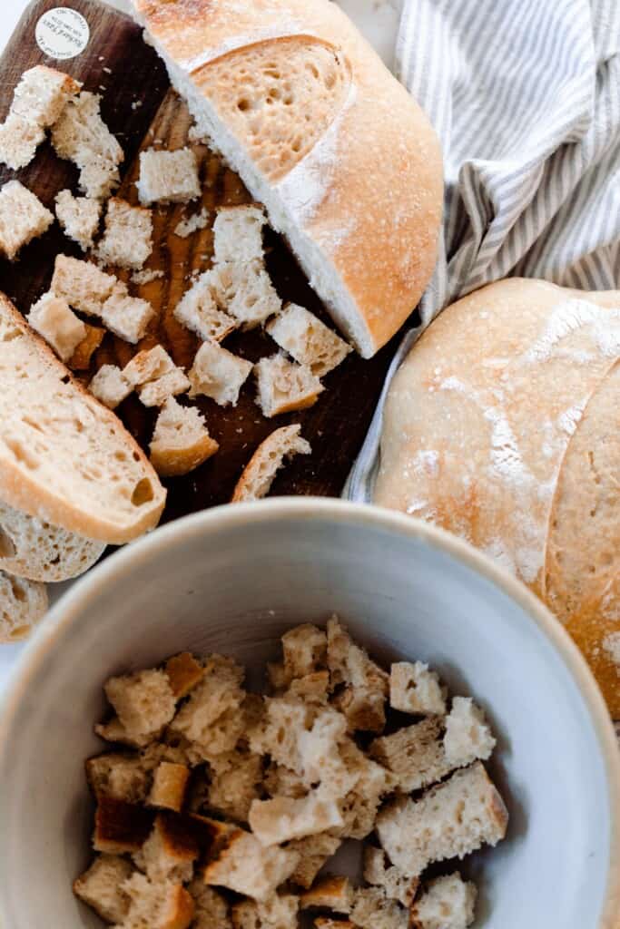bread being cubed on a butting board and placed in a large bowl