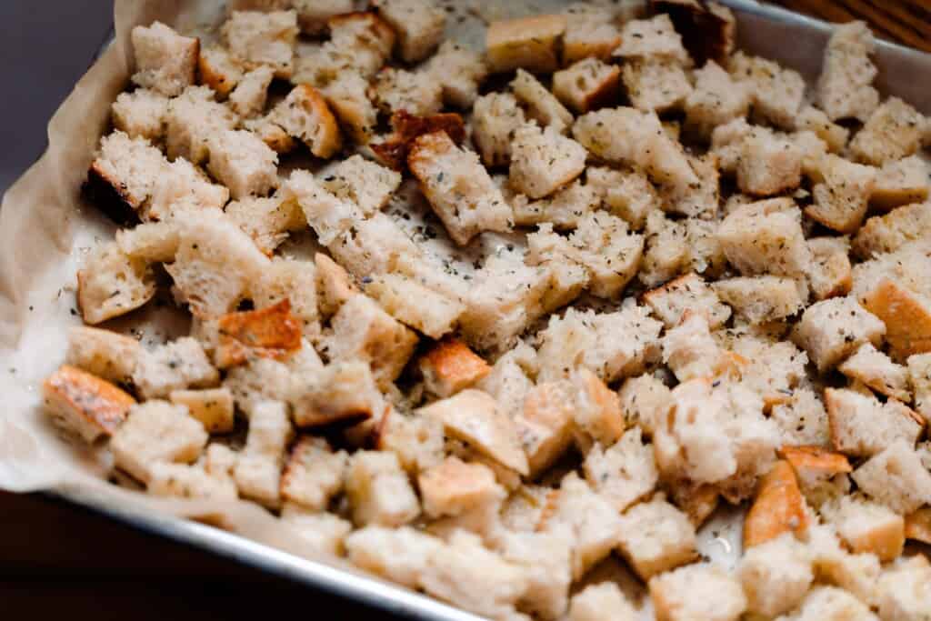 cubed sourdough bread covered in olive oil and herbs on a parchment lined baking sheet