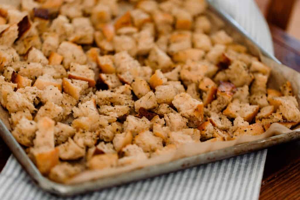 sourdough croutons on a parchment lined baking sheet on a grey and white stripped towel