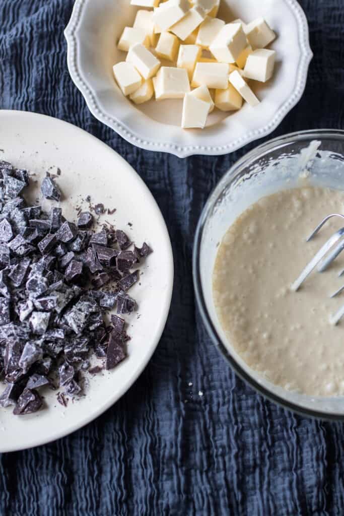 sourdough scone batter in a glass bowl with a plate full of chocolate chunks of another small bowl of cubbed butter