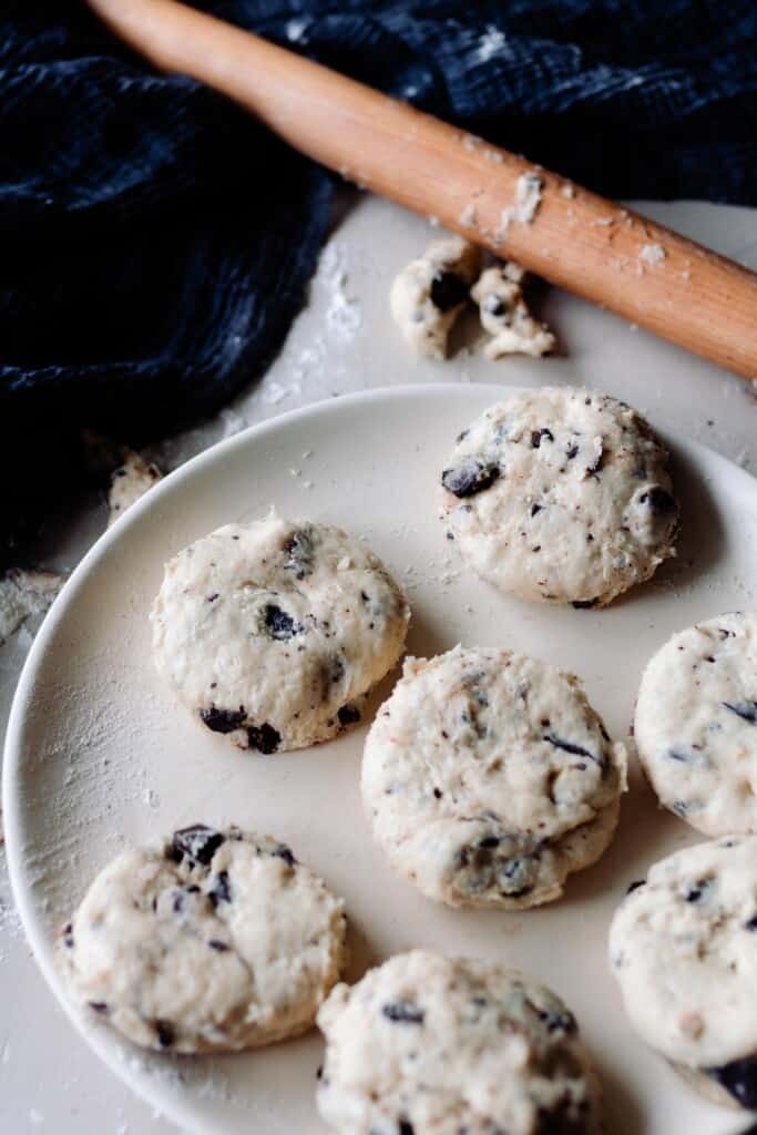 chocolate coconut sourdough scones on a cream colored plate with a rolling pin on a blue towel .