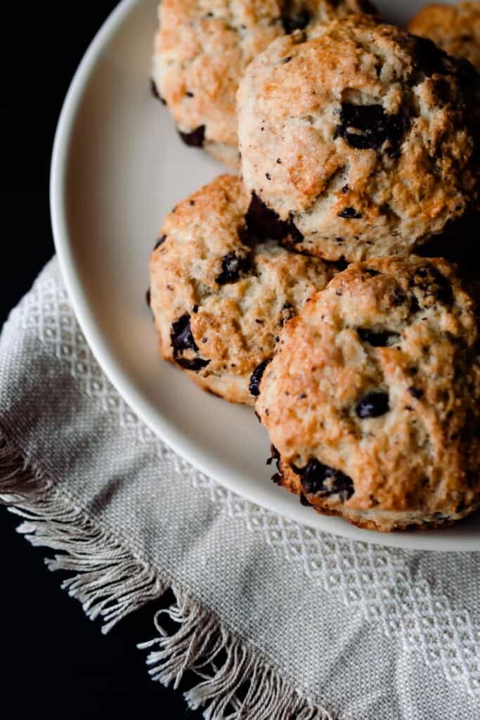 golden chocolate and coconut sourdough scones on a cream colored plate on top of a cream colored towel